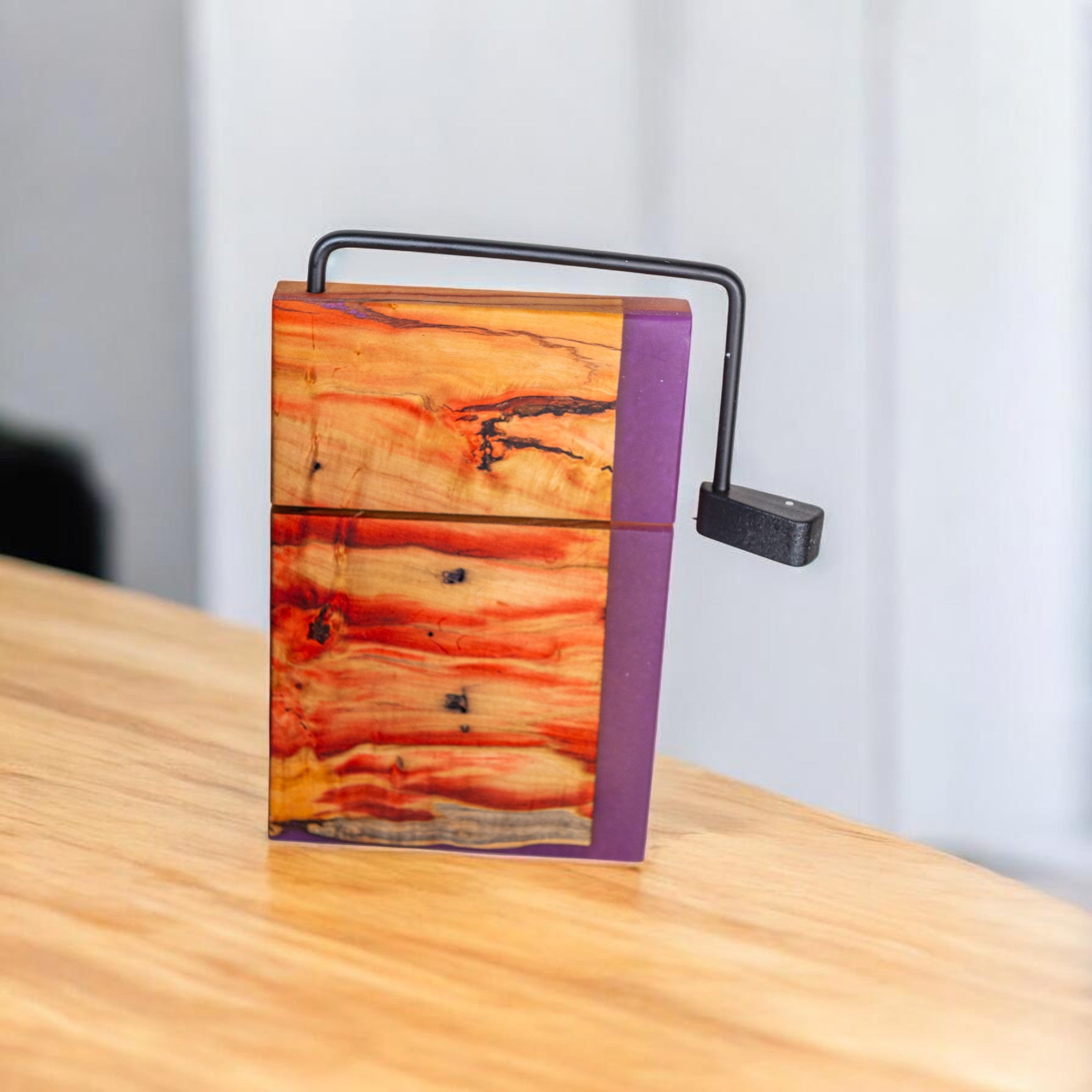 Purple epoxy edge Box Elder wood cheese slicer on wooden surface with metal handle