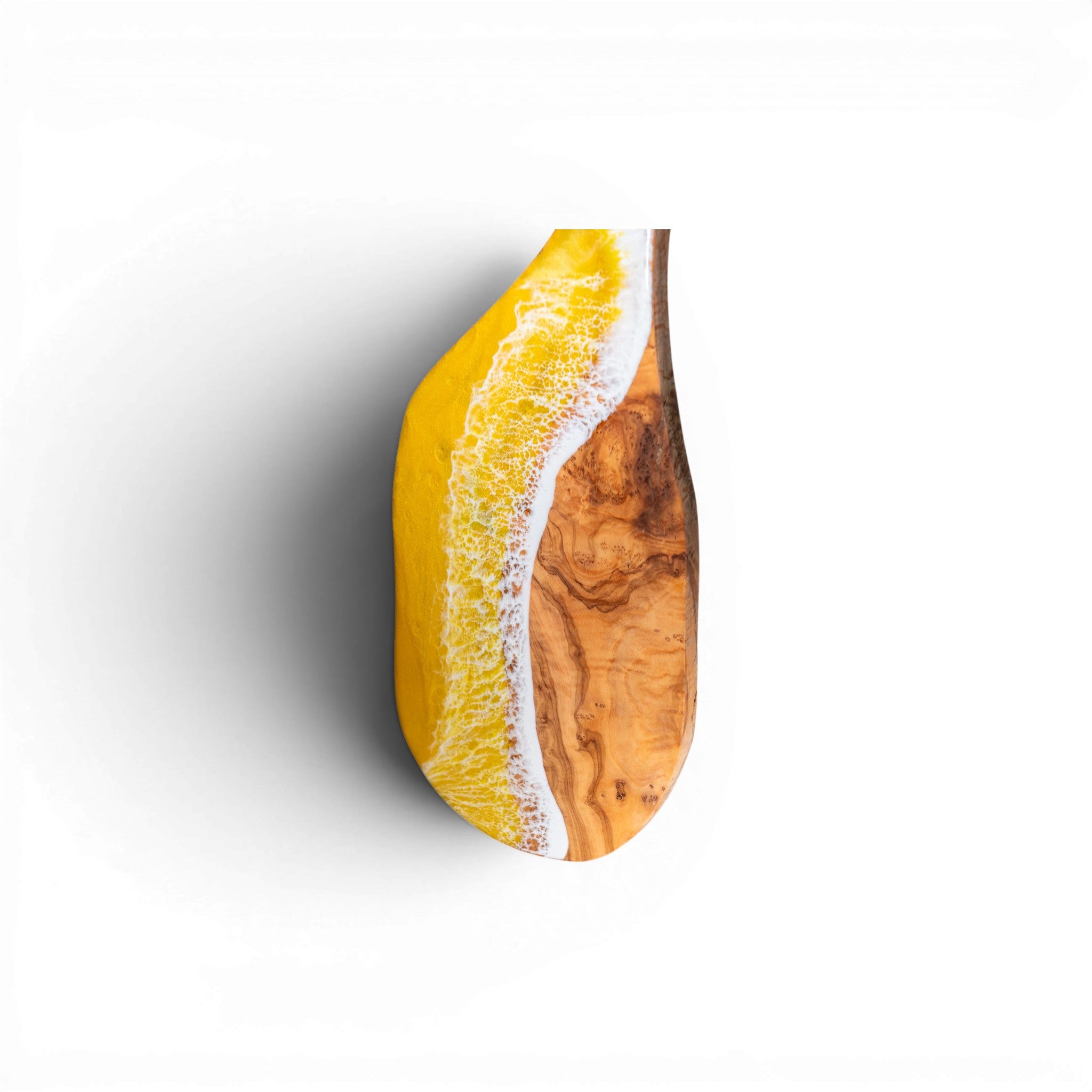 Close-up of textured yellow and white epoxy wave on olive wood cutting board