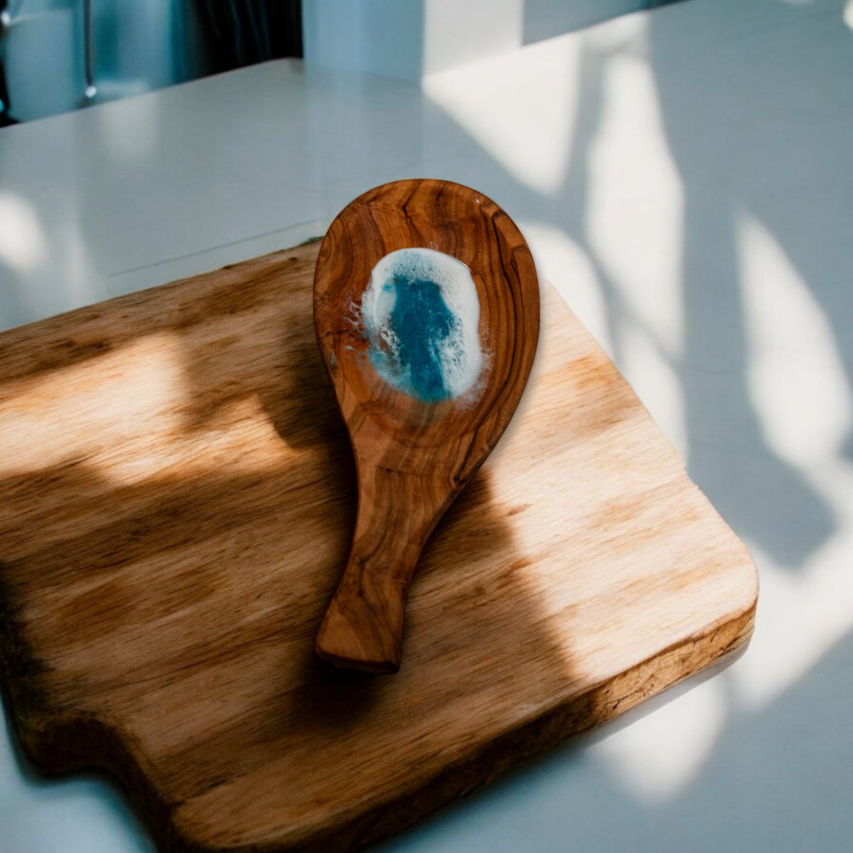 Handmade olive wood spoon rest with embedded blue ocean wave resin on rustic cutting board