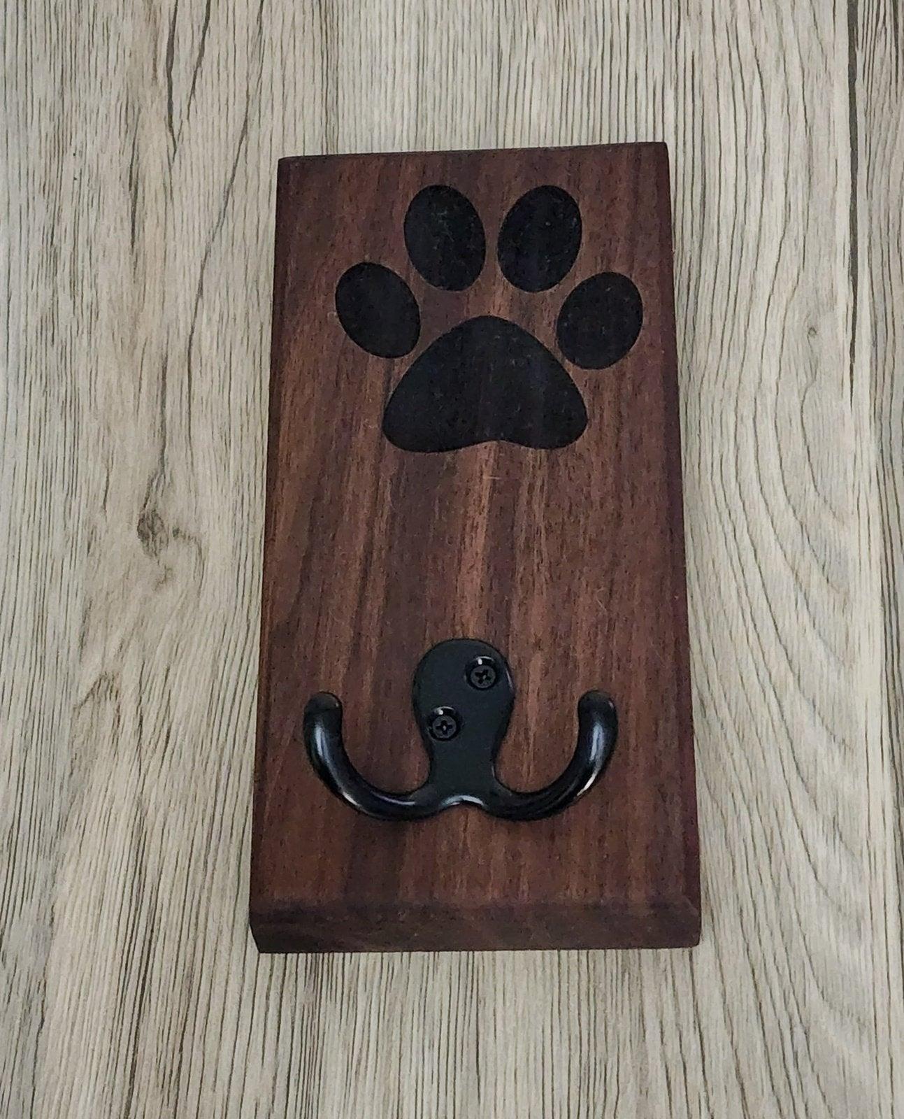 Dark wood dog leash wall mount featuring black metal hooks and paw print engraving