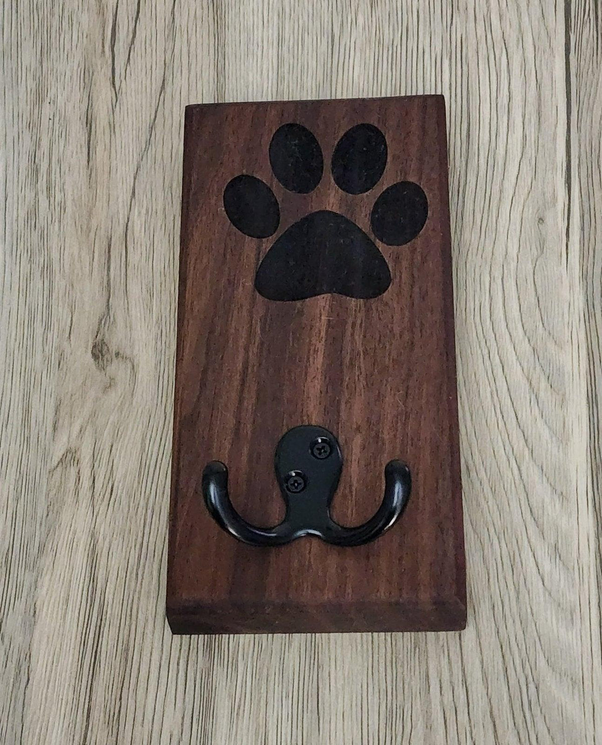 Dark wood dog leash wall mount featuring black metal hooks and paw print engraving