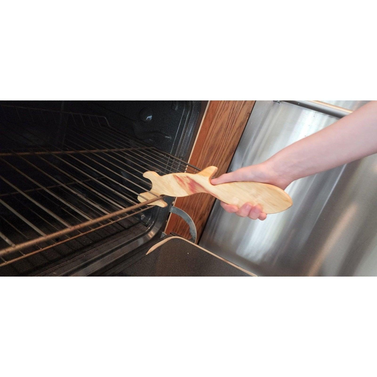 Hand using light walnut squirrel oven rack puller to remove hot rack