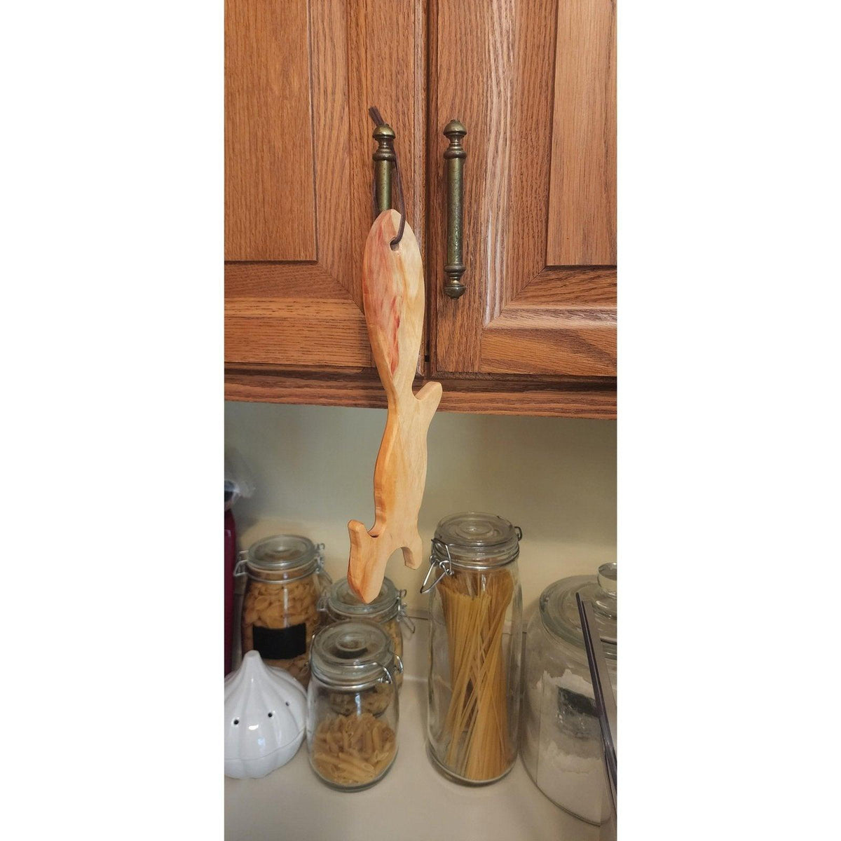 Wooden squirrel oven rack puller hanging from cabinet knob in kitchen