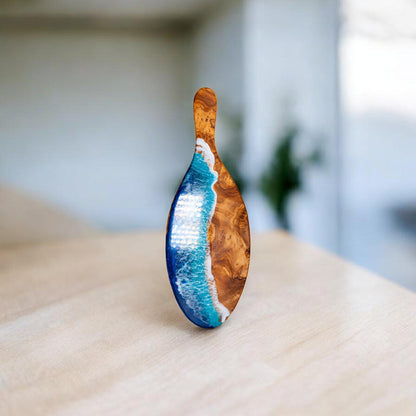 Handcrafted olive wood board with vibrant blue ocean wave epoxy inlay and cutout handle