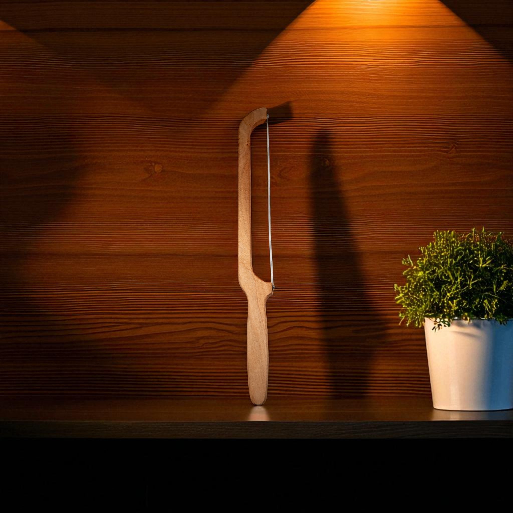 Handmade maple wood bow bread knife on dark shelf with green plant