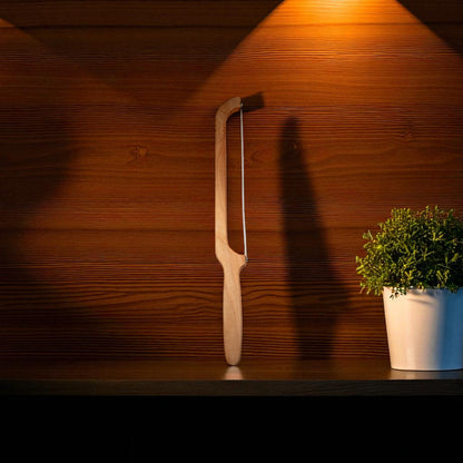 Handmade maple wood bow bread knife on dark shelf with green plant