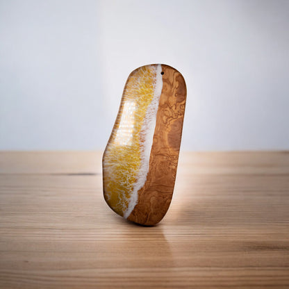 Upright yellow resin ocean wave olive wood serving board on light wood surface
